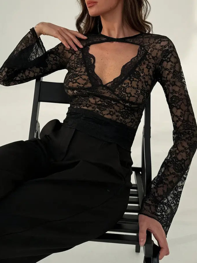 Woman wearing a black lace top and black pants sitting on a chair against a white background
