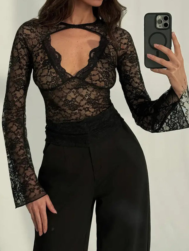 Woman wearing a black lace top and black pants, taking a selfie.